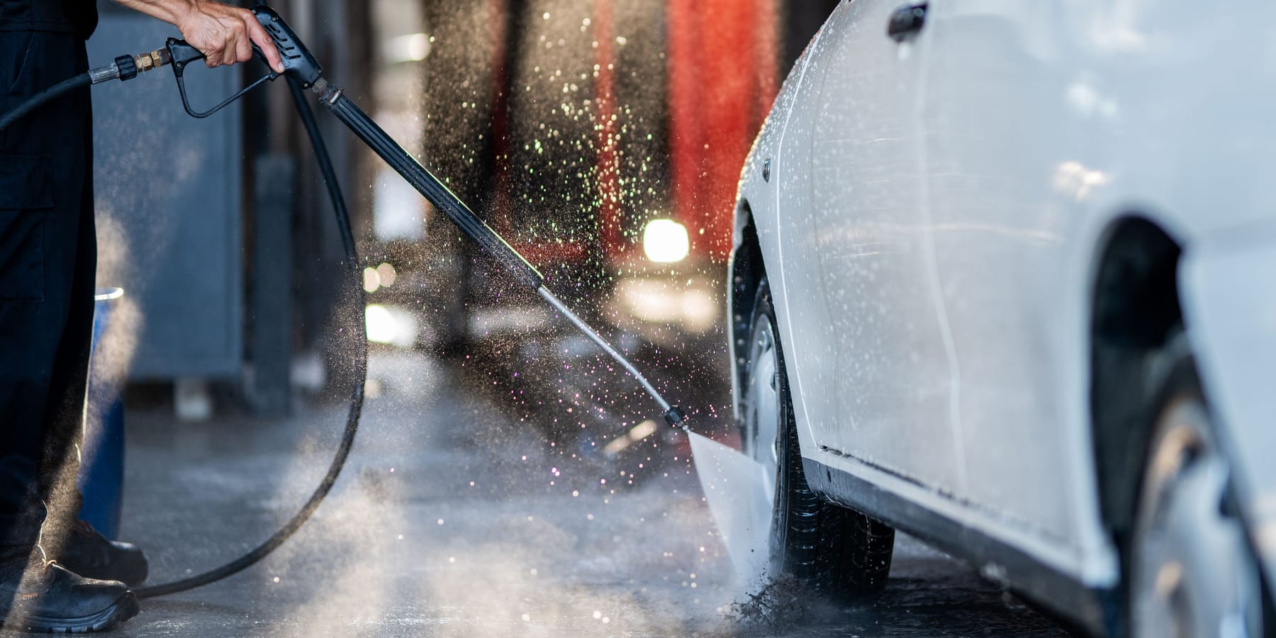 Pistola de agua a presión lavando el lateral de un coche blanco