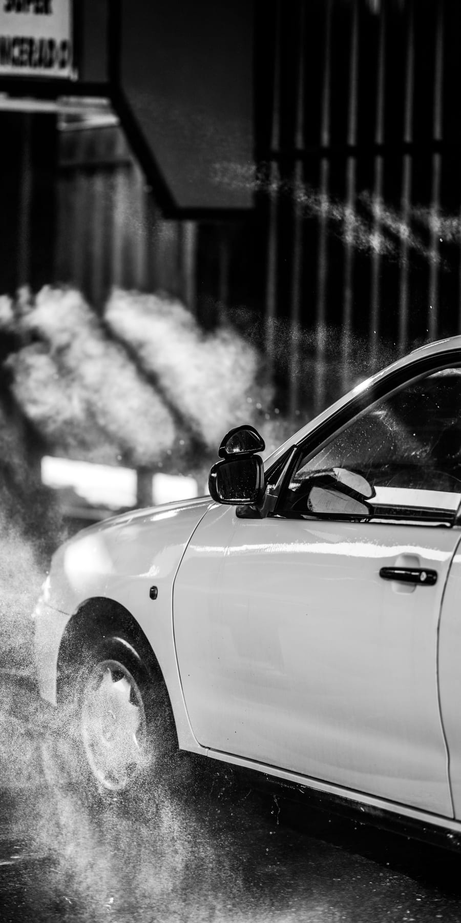 Coche blanco rodeado de agua pulverizada, en blanco y negro