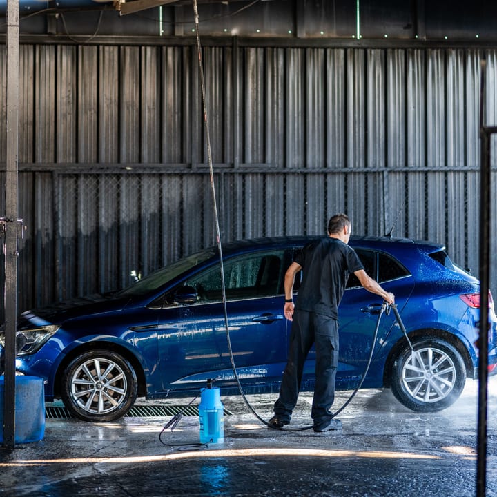 Operario lavando un coche azul en el túnel de lavado